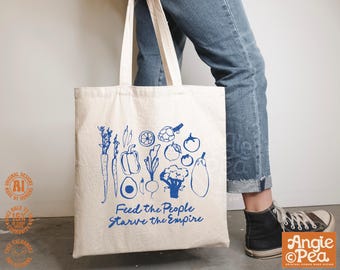 Könnte beinhalten: Eine cremefarbene Canvas-Tragetasche mit einem blauen Grafikdruck verschiedener Gemüsesorten wie Karotten, Paprika und Brokkoli. Unter dem Gemüse steht der Text Feed the People Starve the Empire in einer blauen, handschriftlichen Schrift.