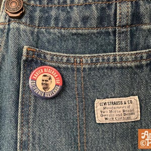 May include: Close-up of blue denim overalls with a pocket. A round button with "Xavier Becerra for California Governor" text and a portrait is pinned on the pocket. A Levi Strauss & Co. label is visible.