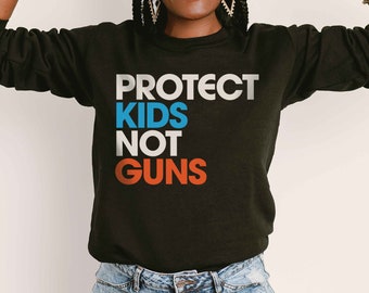 Può includere: Felpa nera con la scritta "PROTECT KIDS NOT GUNS" in lettere bianche, blu e arancioni.