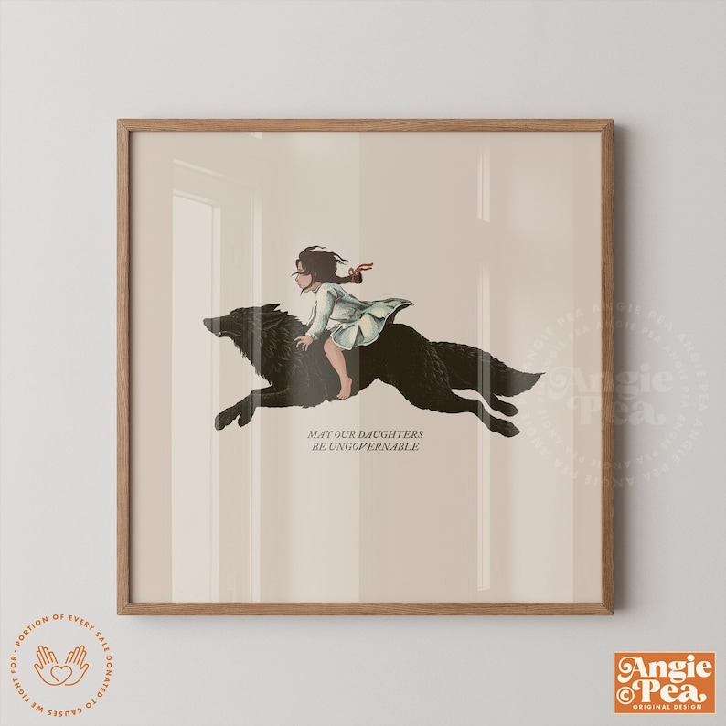 May include: A framed art print featuring a girl riding a black wolf. The girl wears a light green dress. The text "MAY OUR DAUGHTERS BE UNGOVERNABLE" is below the wolf. The print has a beige background and a wooden frame.
