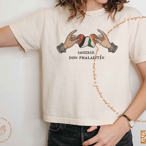 May include: A white t-shirt with a graphic of two hands holding a heart with the flags of Palestine and Ireland. The text "SAOIRSE DON PHALAISTÍN" is printed below the graphic.