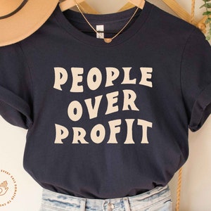 May include: A navy blue t-shirt with the text "PEOPLE OVER PROFIT" printed in a cream color. The shirt has a crew neck and short sleeves.