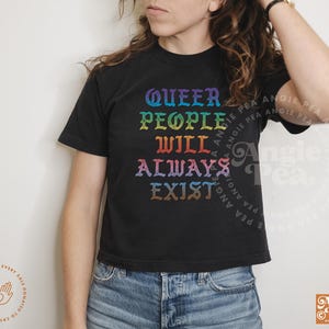 May include: A black cropped t-shirt with the text "Queer People Will Always Exist" in rainbow colors. The text is in a gothic font.
