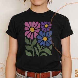 May include: A black t-shirt with a floral design featuring pink, purple, and blue flowers with yellow centers. The flowers are stylized and have a retro feel.