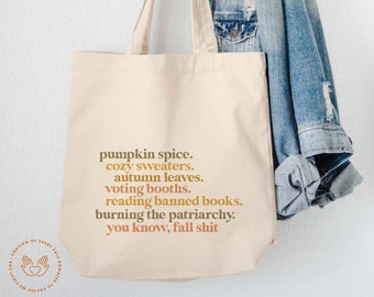 May include: A beige tote bag with a brown and orange graphic print that says "pumpkin spice. cozy sweaters. autumn leaves. voting booths. reading banned books. burning the patriarchy. you know, fall shit"
