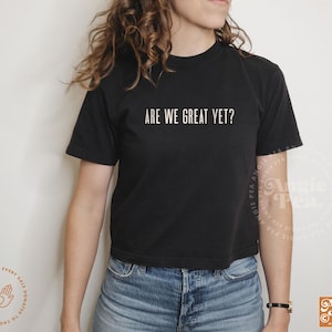 May include: A black cropped t-shirt with the text "ARE WE GREAT YET?" in white lettering.
