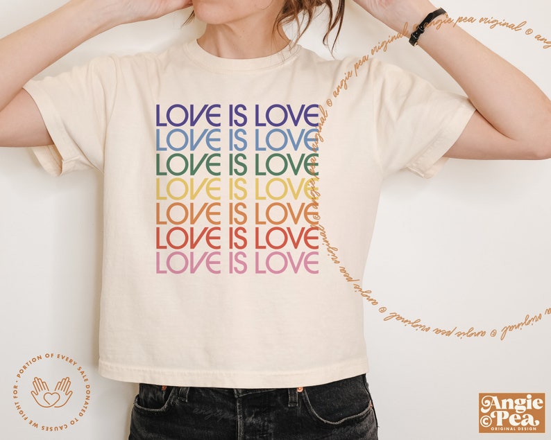 May include: A white t-shirt with the phrase "Love is Love" repeated in rainbow colors. The shirt is cropped and has short sleeves.