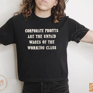 May include: A black cropped t-shirt with white text that reads "Corporate Profits Are The Unpaid Wages Of The Working Class".