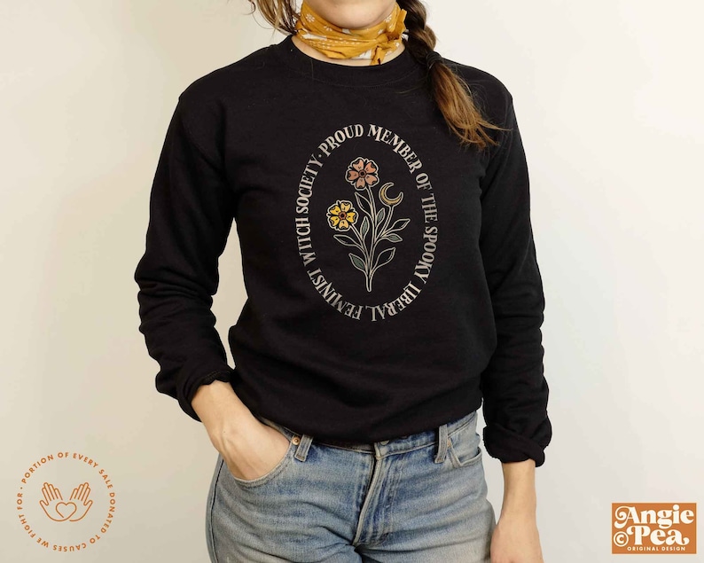 K&ouml;nnte beinhalten: Schwarzes Langarmshirt mit einem runden Grafikdesign mit einem floralen Motiv, einem zunehmenden Mond und dem Text "Proud Member of the Spooky Liberal Feminist Witch Society".
