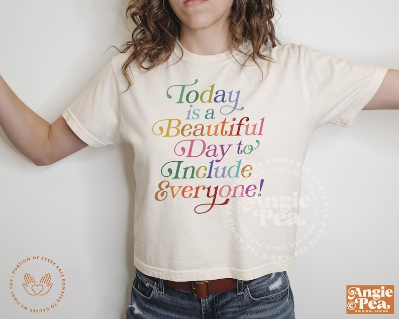 May include: A white cropped t-shirt with the text "Today is a Beautiful Day to Include Everyone!" printed in rainbow colors.