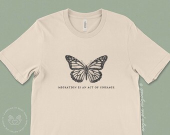 May include: A beige t-shirt with a black and white butterfly graphic and the text "Migration is an act of courage".