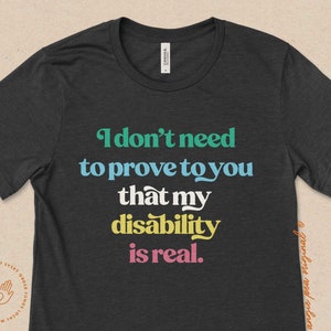 May include: A dark gray t-shirt with the text "I don't need to prove to you that my disability is real." printed in colorful letters.
