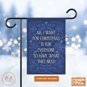 May include: A navy blue garden flag with the text "ALL I WANT FOR CHRISTMAS IS FOR EVERYONE TO HAVE WHAT THEY NEED" in white. The flag has a floral design in blue and is displayed on a black metal stand.