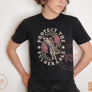 May include: Black t-shirt with a circular graphic that reads "Protect the Vulnerable" around a rabbit and flowers. The text "Resist Tyranny" is on the rabbit. The shirt has short sleeves and a crew neck.
