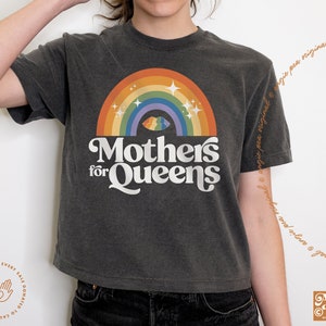 May include: A dark gray cropped t-shirt with a rainbow and a stylized text design that reads "Mothers for Queens".