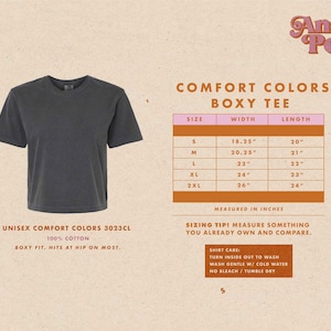 May include: A size chart for a unisex boxy tee shirt made by Comfort Colors. The chart shows the width and length measurements in inches for sizes S, M, L, XL, and 2XL. The text "Unisex Comfort Colors 3023CL 100% Cotton Boxy Fit. Hits at hip on most." is also included.