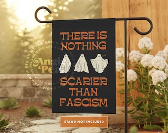 May include: Black Halloween garden flag with orange text reading "THERE IS NOTHING SCARIER THAN FASCISM". Three white ghost illustrations are below the text. The flag is displayed on a black metal stand. The words "STAND NOT INCLUDED" are at the bottom.