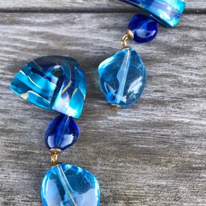 May include: A blue and gold beaded necklace with various shapes and sizes of beads. The necklace features a mix of translucent and opaque beads in shades of blue and gold, connected by gold-colored metal findings.