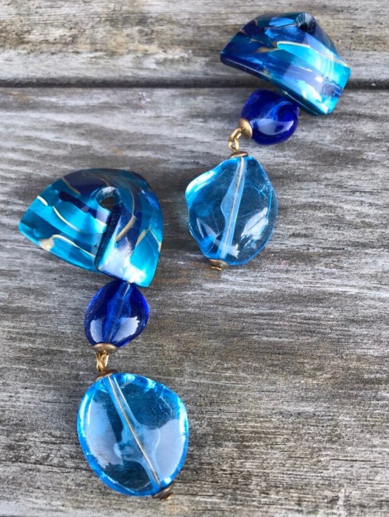 May include: A blue and gold beaded necklace with various shapes and sizes of beads. The necklace features a mix of translucent and opaque beads in shades of blue and gold, connected by gold-colored metal findings.