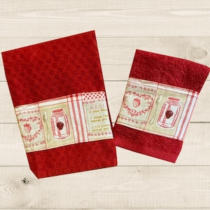 May include: Two red kitchen towels with a white and beige patterned border. The border features a heart, a spoon, and a jar with a strawberry inside. The text "RECIPE" is visible on the larger towel.