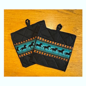 Può includere: Due presine da forno imbottite nere con un bordo a motivi turchese e arancio che presenta un design di cavalli che corrono.