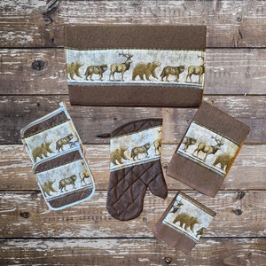 Op de afbeelding: Set van vijf bruine keukendoeken met een print van bosdieren. De doeken tonen beren, herten en wolven. Twee van de doeken zijn ovenwanten.
