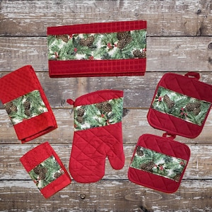 May include: Set of red kitchen towels and pot holders with a pine cone and evergreen print. The set includes two tea towels, one oven mitt, and two pot holders.