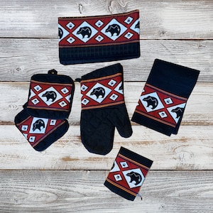 May include: Set of black kitchen towels and pot holders with a red, white, and black geometric pattern featuring a bear silhouette.