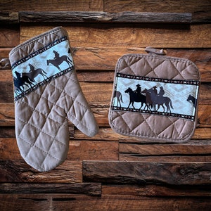 May include: A set of two brown quilted kitchen pot holders with a white and brown patterned trim featuring a silhouette of cowboys riding horses.