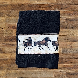 May include: Black bath towel with a white border featuring a brown and black horse design.