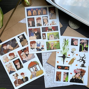 May include: Three art prints featuring comic-style illustrations. The prints showcase various scenes with characters in different settings. The color palette includes browns, reds, and whites. The prints are on a brown surface with envelopes.