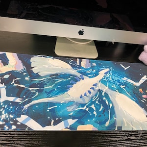 Puede incluir: Una alfombrilla de escritorio rectangular con una vibrante ilustraci&oacute;n de una gran criatura blanca similar a un drag&oacute;n volando sobre un oc&eacute;ano azul profundo con patrones de agua arremolinados y formas geom&eacute;tricas abstractas de fondo.