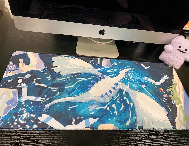 Puede incluir: Una alfombrilla de escritorio rectangular con una vibrante ilustraci&oacute;n de una gran criatura blanca similar a un drag&oacute;n volando sobre un oc&eacute;ano azul profundo con patrones de agua arremolinados y formas geom&eacute;tricas abstractas de fondo.