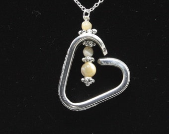 May include: A silver heart-shaped pendant necklace with a chain and three white and cream-colored beads hanging inside the heart.