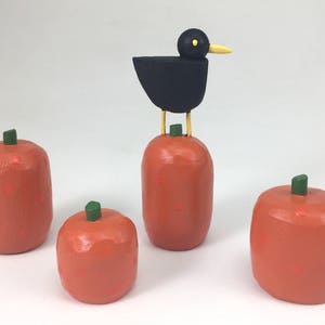 Pode incluir: Quatro abóboras laranja com caules verdes, uma com um pássaro preto em cima. O pássaro tem um bico e pernas amarelas.