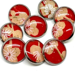 May include: A set of ten red and white buttons with a floral design. The buttons are round and have a silver metal rim.