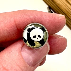 May include: A silver-toned button with a black and white panda bear image on a green background.