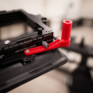 May include: A red plastic lever with a black knob and a black metal frame. The frame has the text "LMB 4x5 Basic Module" and "K2.0014006" printed on it.