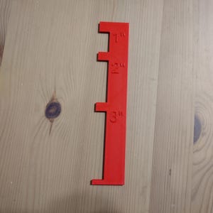 May include: A red plastic ruler with markings for 1 inch, 2 inches, and 3 inches.