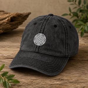 Könnte beinhalten: Eine anthrazitfarbene Baseballkappe mit verwaschener Optik. Auf der Vorderseite befindet sich ein weißes, gesticktes kreisförmiges geometrisches Muster, bekannt als Blume des Lebens, das aus mehreren überlappenden Kreisen in symmetrischer Anordnung besteht.