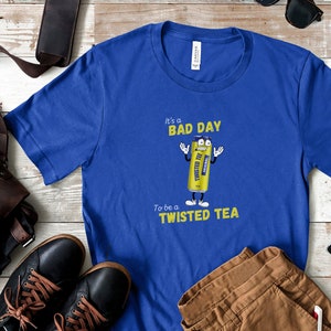 May include: A blue t-shirt with a yellow cartoon can of Twisted Tea. The can has a face and arms and is holding up two fingers. The text on the shirt reads "It's a bad day to be a Twisted Tea."