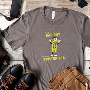 May include: A gray t-shirt with a yellow graphic of a Twisted Tea can with the text "It's a bad day to be a Twisted Tea".