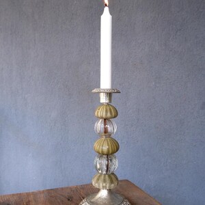 May include: A tall, silver candlestick with a white candle lit at the top. The candlestick is decorated with sea urchin shells and clear glass beads. The base is ornate, and the candle is lit with a small flame.