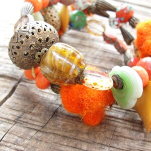 May include: A colorful bracelet with beads of various materials, including glass, metal, and fabric. The bracelet features a mix of orange, green, brown, and white beads.