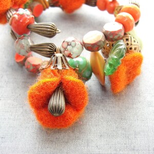 May include: A close-up of a colorful bracelet made with orange, green, and brown beads. The bracelet has a large orange felt flower charm attached to it.