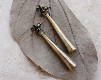 May include: A pair of gold-toned earrings with a floral design and a long, tapered drop. The earrings are displayed on a dried leaf.