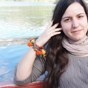 May include: A woman with long brown hair wearing a gray sweater and a light brown scarf. She is wearing a colorful beaded bracelet on her wrist.