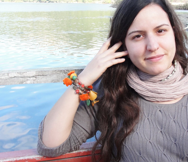 May include: A woman with long brown hair wearing a gray sweater and a light brown scarf. She is wearing a colorful beaded bracelet on her wrist.