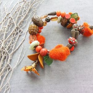 May include: Orange and brown beaded bracelet with felt accents. The bracelet features a variety of beads, including glass, metal, and wood.