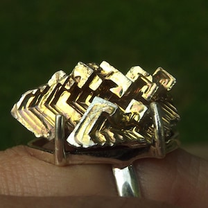 May include: A silver ring with a large, gold-colored, geometric crystal set in the center. The crystal is faceted and has a unique, abstract design.
